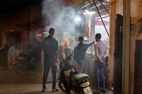 Nocturnal street scene with people, smoke from cooking areas and scooters in a busy area