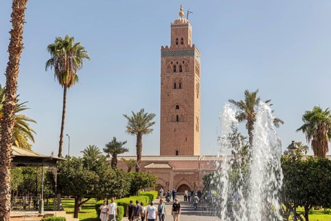 The Koutoubia Mosque in Marrakech with palm trees and a fountain in a sunny garden, visited by