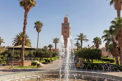 A well-kept garden with a sparkling fountain in front of the majestic Koutoubia Mosque on a sunny