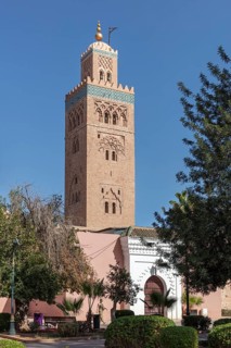 High tower of the Koutoubia Mosque against a blue sky surrounded by trees