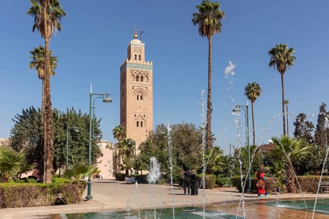View of the Koutoubia Mosque with bubbling fountains and palm trees against a blue sky