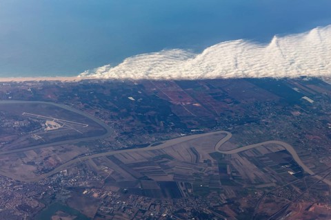 Aerial view of a coastal landscape with waves, agricultural fields and an airport