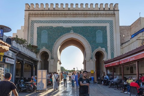 Historic gate with mosaics, people strolling along shops