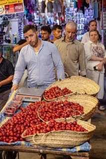 People taste and sell fresh fruit in baskets at a busy market