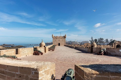 Large stone wall of a fortress with cannons and a wide view of the sea on a clear, sunny day