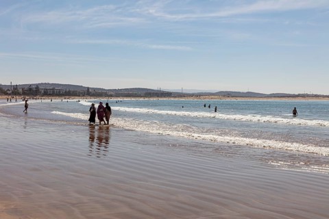 People walking on the beach in shallow water under clear sky