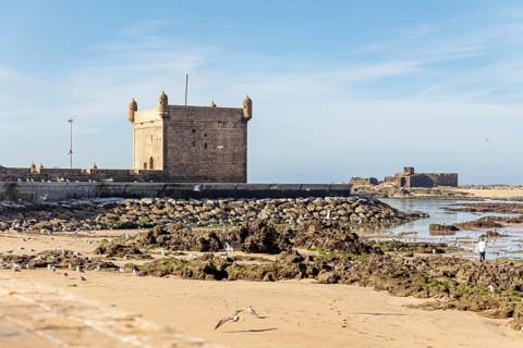 Extensive beach with rocks and historic walls by the sea under clear skies