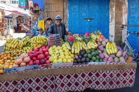 Well-stocked fruit stand with colorful fruits in front of a blue door