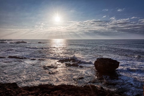 View of the sea at sunset with rocks and waves under a cloudy sky