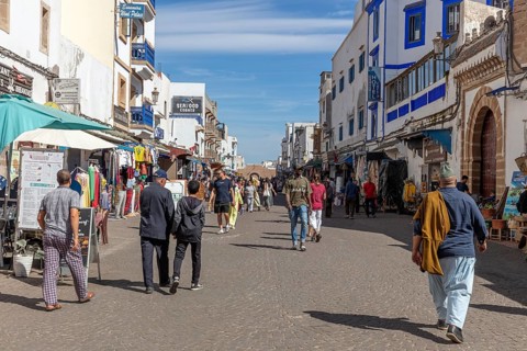 Bustling market street with people and numerous shops under a clear blue sky