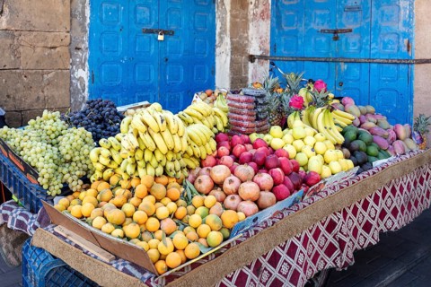 Richly filled fruit stand with colorful fruits in front of a blue door