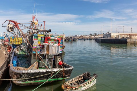 A fishing boat loaded with colorful boxes in the harbor, still water and blue skies