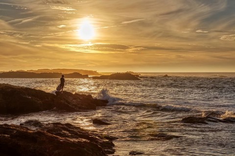 Silhouette of a person on a rock at sunset by the sea