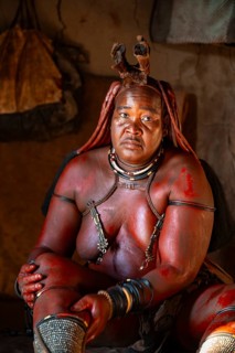 Elderly Himba woman rubbing herself with red paste for skin care, in a hut, traditional Himba