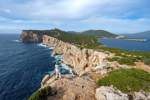 Tourist enjoying the view of steep cliffs by the sea, coastal landscape, cliffs on the Capo Caccia