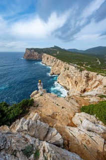 Tourist enjoying the view of steep cliffs by the sea, coastal landscape, cliffs on the Capo Caccia