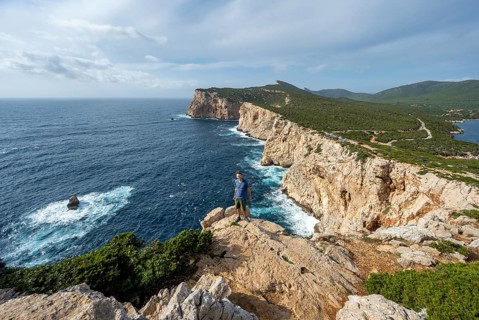 Tourist enjoying the view of steep cliffs by the sea, coastal landscape, cliffs on the Capo Caccia