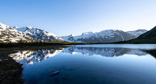 Mountain peaks with Portage Glacier glacier and snow reflected in Divide Lake mountain lake in