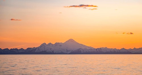 View of Cook Inlet on white mountain peaks of Mount Iliamna at sunset, picturesque golden light of