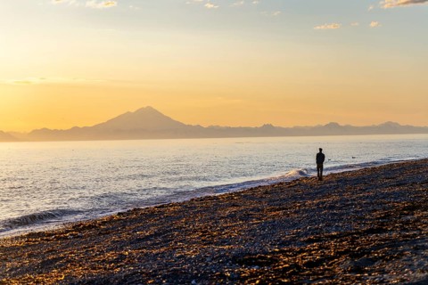 Young man walking along the beach at sunset, view across Cook Inlet to white mountain peaks of