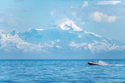 View over Cook Inlet to white mountain peaks of Mount Iliamna, motor boat rides on the ocean,