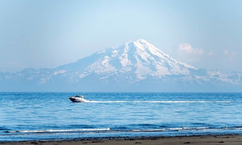 View over Cook Inlet to white mountain peaks of Mount Redoubt, motor boat rides on the ocean,