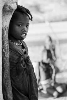 Black and white, Himba girl leaning at a traditional clay hut, in the morning, traditional Himba
