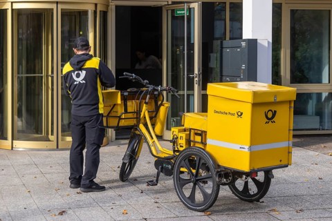 Deutsche Post mailmen on a bicycle through the city. Stuttgart, Baden-Württemberg, Germany