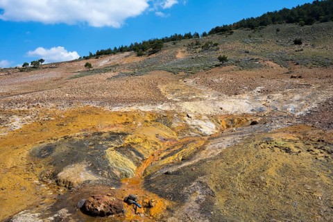 Extensive geological landscape with hills, orange and green areas under blue sky, geothermal area,