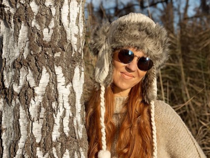 Slender pretty woman with fur hat and sweater, red hair and warm winter colors between birch forest