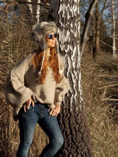 Slender pretty woman with fur hat and pompoms, red hair and warm winter colors between birch forest