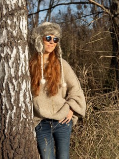 Slender pretty woman with fur hat and sweater, red hair and warm winter colors between birch forest