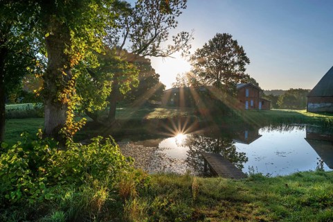 Manor with historic stables and pond, from 1923, in backlight with sun star, Gut Othenstorf,