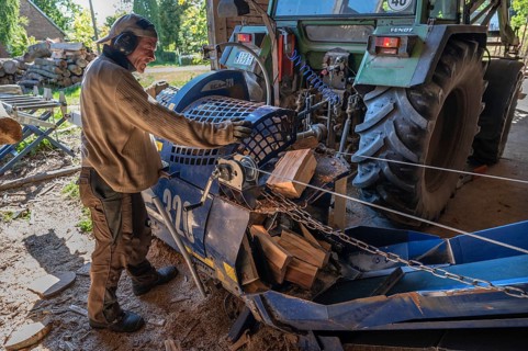 Young man sawing and splitting beech logs with his saw cutting machine, powered by a tractor in a