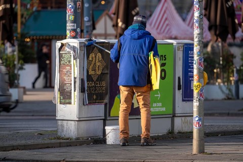 Man sticks posters to electrical boxes near Alexanderplatz, Berlin, Germany