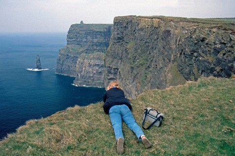 Young woman taking pictures at the edge of a cliff, there was no fence back then, Cliffs of Moher,