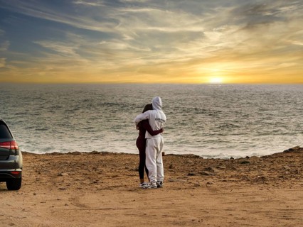 Young couple in love standing on the coast of Farol de Cabo Raso lighthouse, São Bras de Sanxete