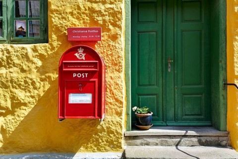 Post office, façade detail, red mailbox with post horn and crown, green wooden door, yellow wall,