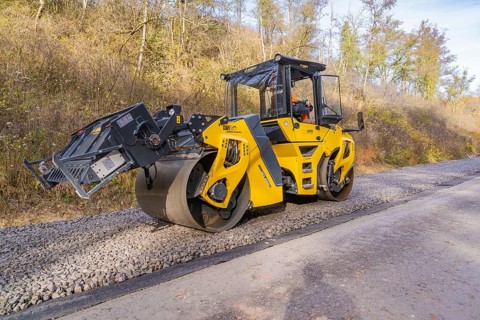 Yellow road roller on gravel road in autumn landscape during construction, track construction of