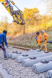 Construction workers supervise the use of an excavator for laying concrete ties, Hermann Hesse
