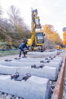 Workers use an excavator to lay concrete blocks along the tracks in autumn surroundings, track