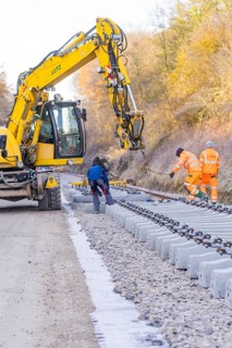 Excavators and workers lay rail blocks on a construction site on an autumn day, track construction