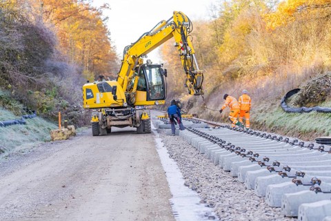 Workers and an excavator lay tracks in an autumn environment, track construction of the Hermann