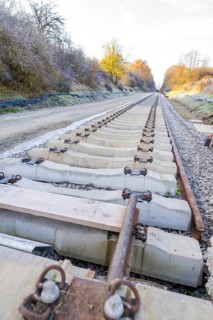 Behind a railroad, a long, straight section of track stretches through autumnal nature, track