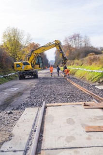 Construction workers lay tracks on a construction site while a yellow excavator assists. Autumn