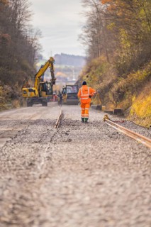 Road construction with construction workers and cranes on a gravel road in autumn, track