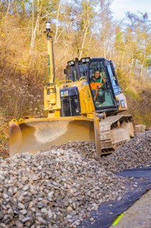 Bulldozer with a large shovel moves gravel on a construction site, track construction of the