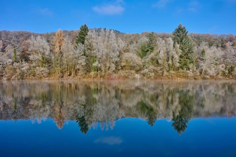 A quiet autumn picture with a lake whose water reflects an autumnal forest, hoarfrost, winter,