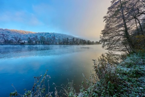A frosty morning on the river with trees and reflecting water in shades of blue and gold,