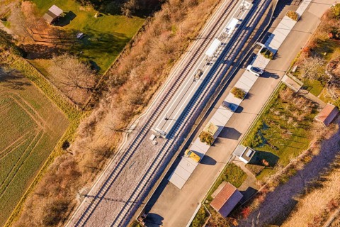 View from above of a train station with an adjacent street and autumnal greenery in the area, new